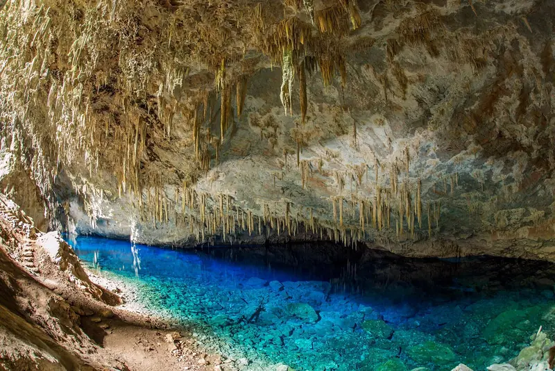 Lago azul no interior da Gruta do Lago Azul, em Bonito, com estalactites no teto e a trilha de pedra à esquerda