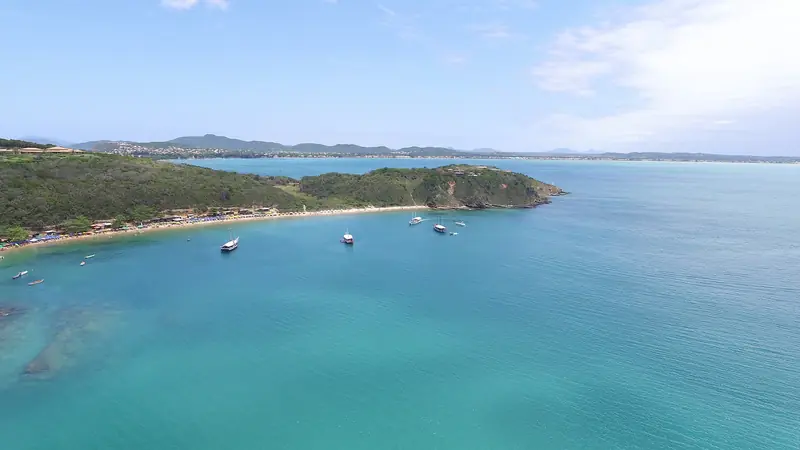 Vista aérea da Praia da Tartaruga, em Búzios, com água verde-turquesa, barcos ancorados e a península ao fundo