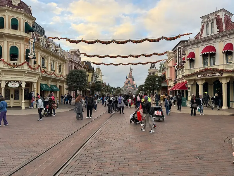 Main Street, U.S.A. enfeitada com guirlandas, com o castelo da Bela Adormecida ao fundo e visitantes na rua