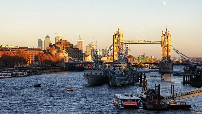 Tower Bridge e o navio HMS Belfast no Tâmisa ao entardecer, com os prédios de Canary Wharf ao fundo