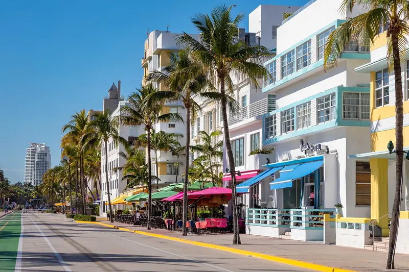 Hotéis art déco brancos com detalhes em azul-turquesa e amarelo, palmeiras e toldos coloridos ao longo da Ocean Drive, em South Beach, sob céu limpo