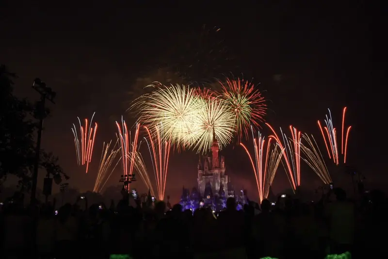Fogos de artifício coloridos sobre o castelo da Cinderela iluminado, no Magic Kingdom, com o público em silhueta