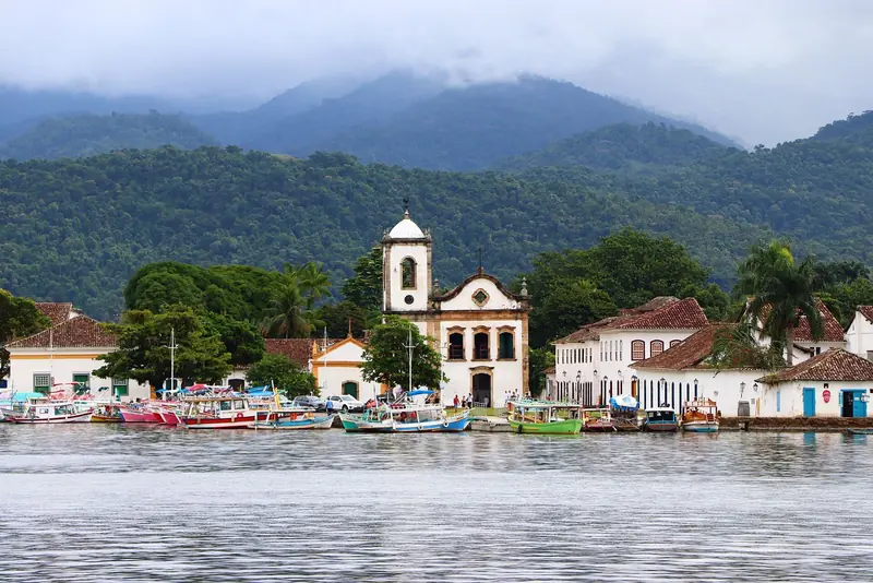 Igreja de Santa Rita vista da baía de Paraty, com barcos atracados e a serra coberta de mata ao fundo